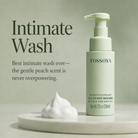 TOSOYOYA Intimate Wash pump bottle in a pale mint green color, displayed next to a dollop of white foaming mousse on a round marble pedestal against a matching sage green background with product text.